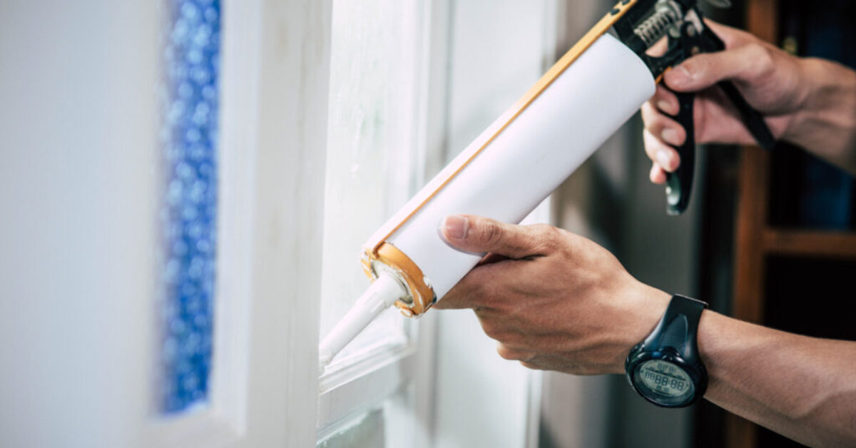 Applying mastic sealant around a window to improve insulation.